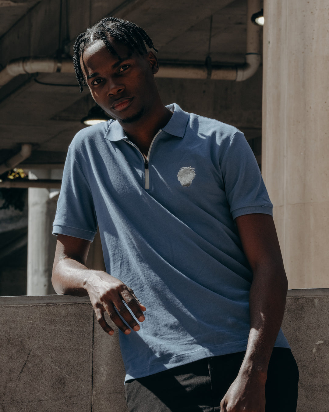 Person wearing a blue polo shirt with a logo, standing in an industrial setting.  #color_steel-blue