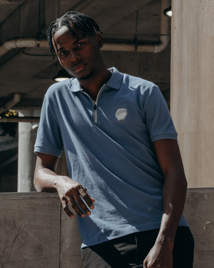 Person wearing a blue polo shirt with a logo, standing in an industrial setting.  #color_steel-blue