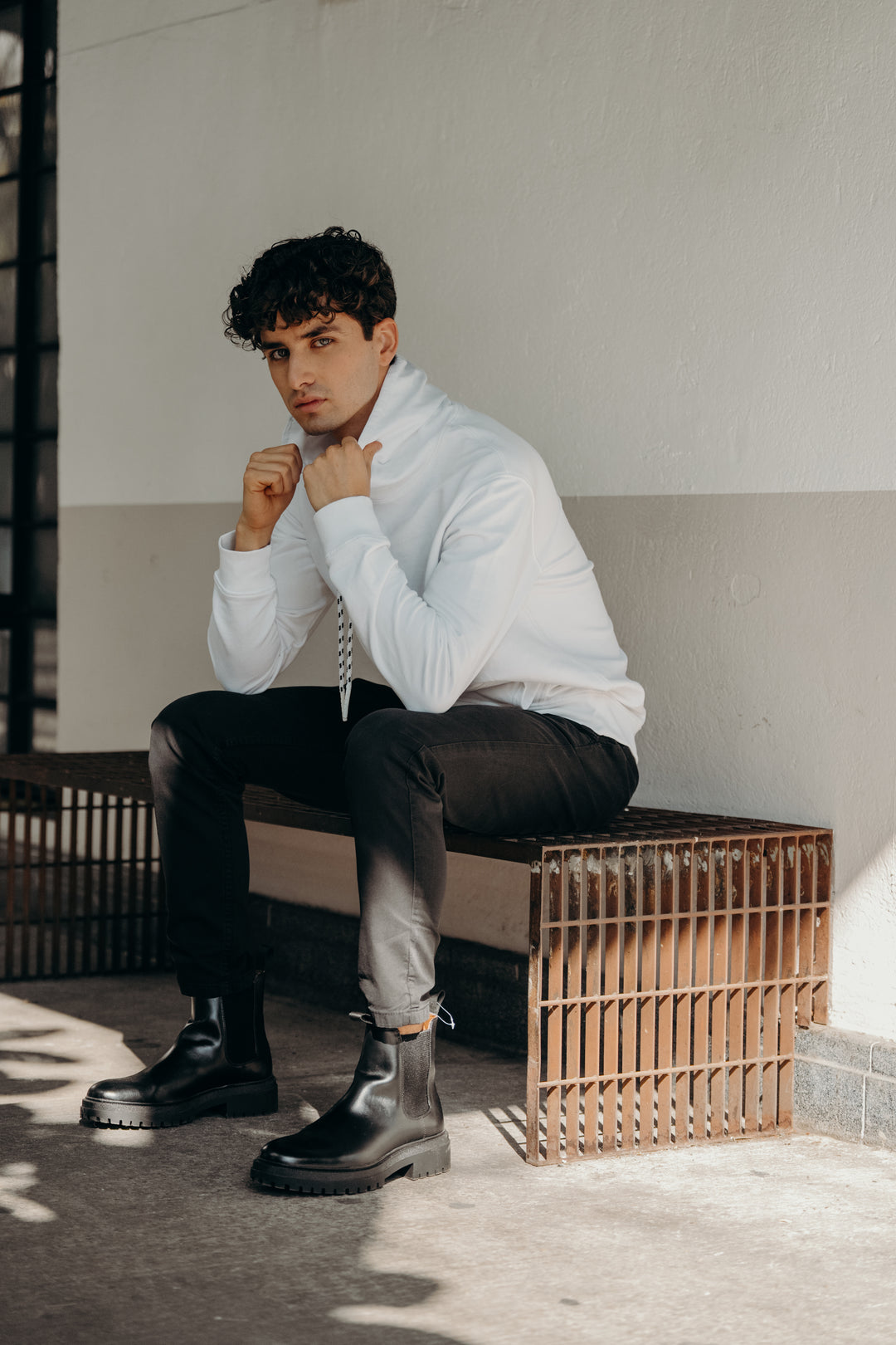 Man sitting on a bench wearing a white shirt, black pants, and black boots. #color_white