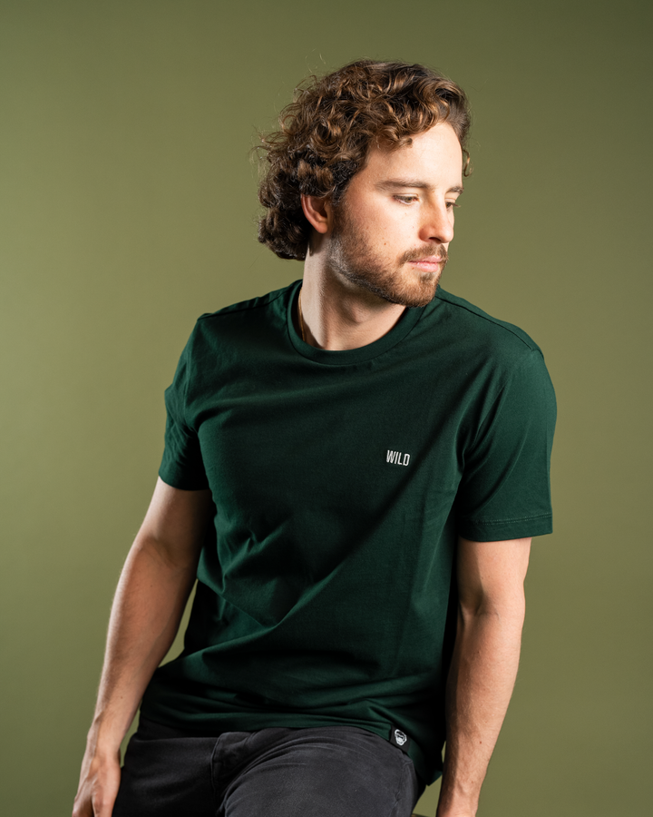 Man wearing a dark green t-shirt with 'WILD' logo against a green background #color_gunmetal-green