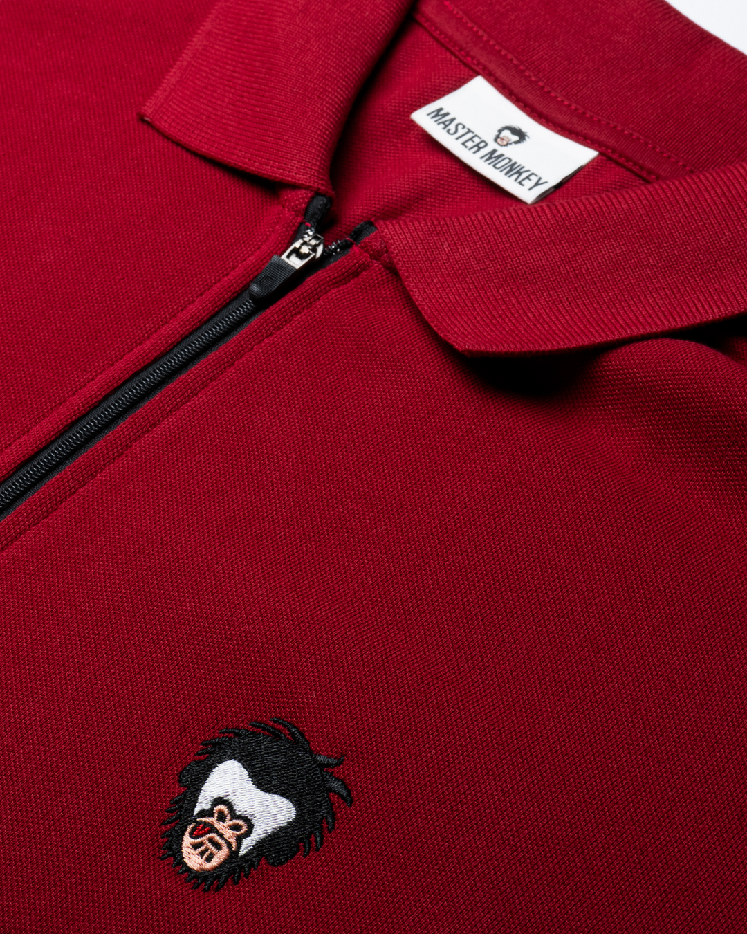 Close up of red-colored polo with black zipper, Master Monkey logo in the wearer's left chest #color_brick