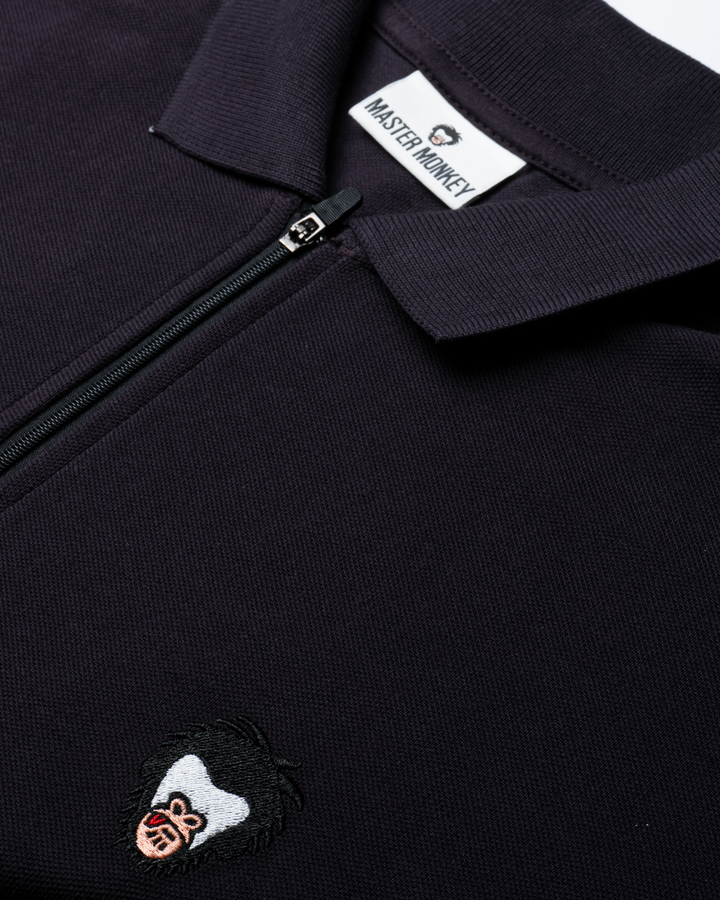 Close up of the zip up polo with the Master Monkey logo in Lead #color_lead