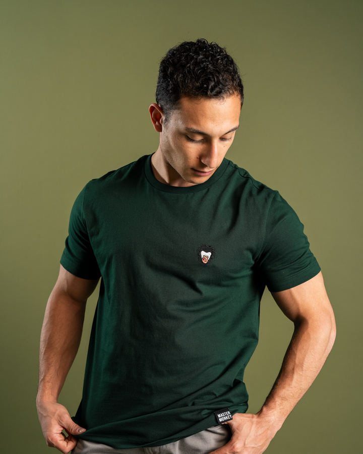 Man wearing a dark green t-shirt with a small logo on a solid background, Master monkey logo #color_gunmetal-green