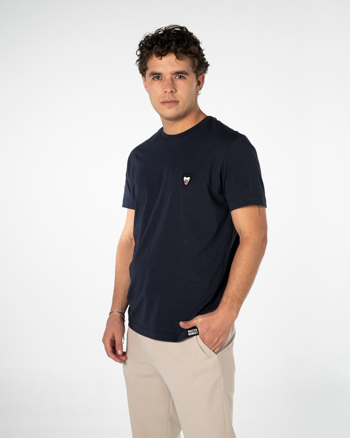 Man wearing a navy blue t-shirt with a small Master Monkey logo on a white background #color_midnight