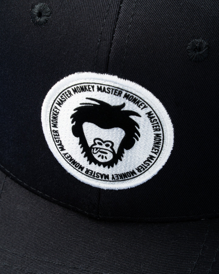 Black cap with a white embroidered patch featuring a logo and text on a dark background #color_black